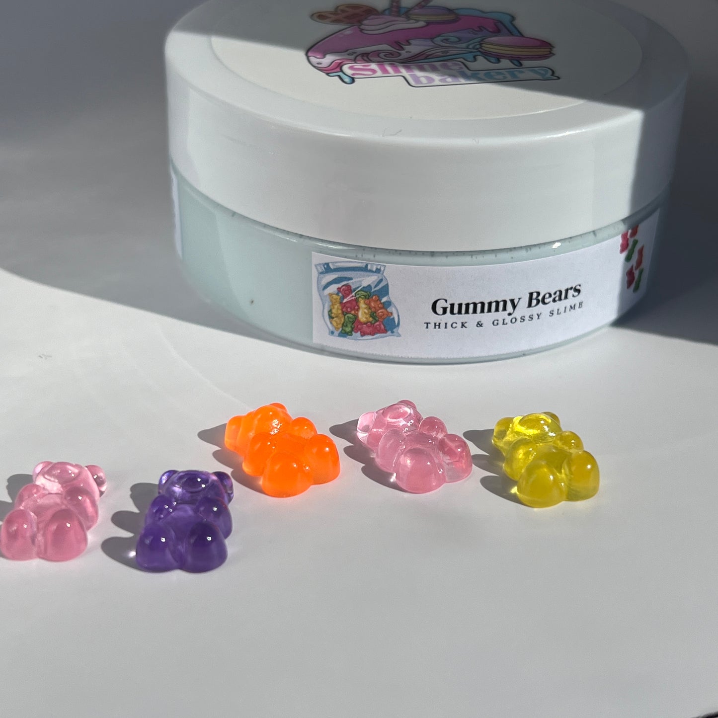 Glossy light blue slime with a thick, smooth texture, adorned with vibrant multi-coloured acrylic gummy bear charms. Provides a fun, sensory-rich experience with a sweet aroma.